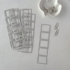 Metal dies shaped like film strips on a light gray surface with a small container of clips.
