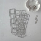 Stack of small metal frames on a light gray surface with a white dish containing clips and a paperclip.