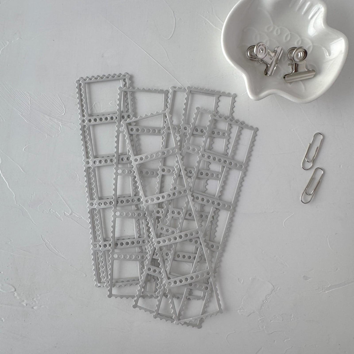 Stack of grey Frames Vol. 1 frame cards with a white dish of clips and a paperclip