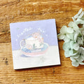 Notebook with a tea cup illustration on a wooden surface with flowers