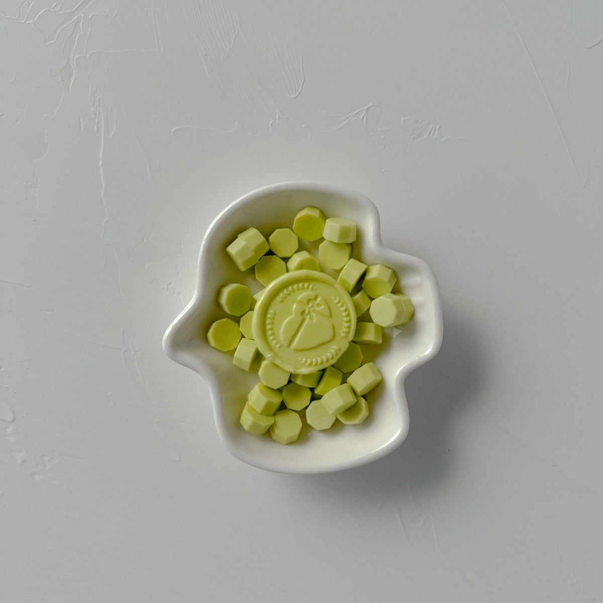 Fresh Sprout sealing wax beads in a bright leafy green shade piled in a white dish on a grey backdrop