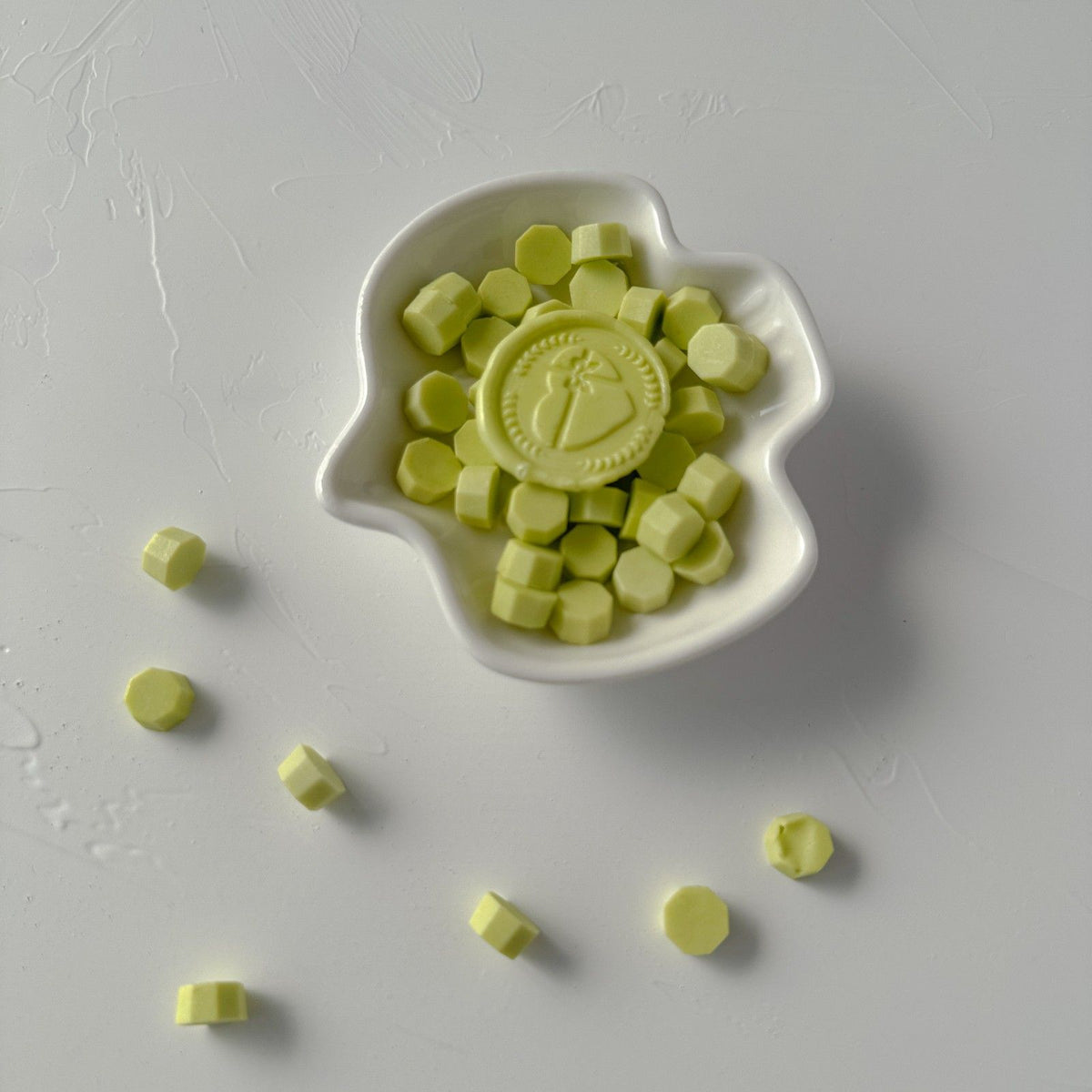 Close-up of a white dish of Fresh Sprout Wax Beads showing their fresh green tone on a grey surface