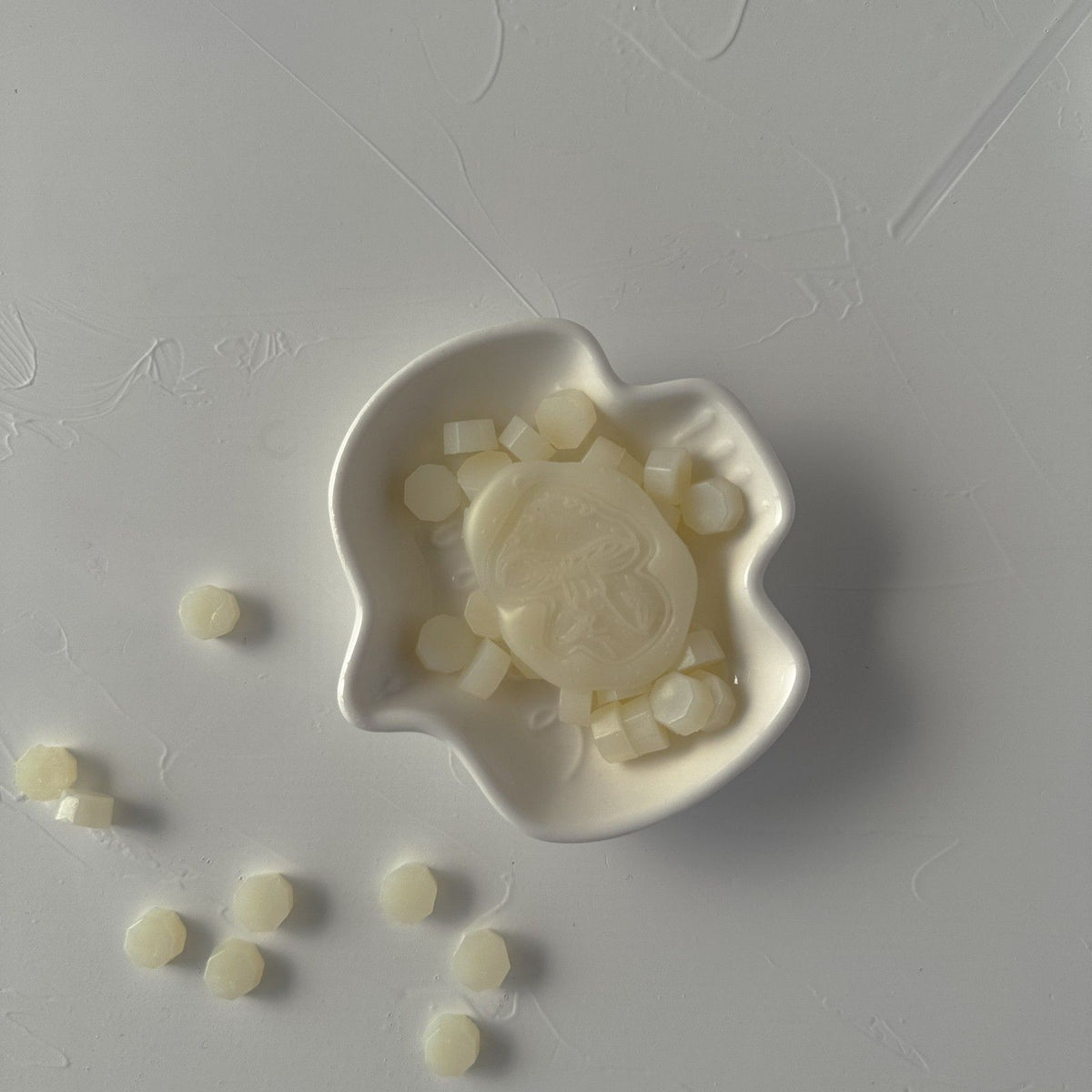 Frosted Ivory Wax Beads shown with a star-design seal mold on a grey surface, soft shimmering detail