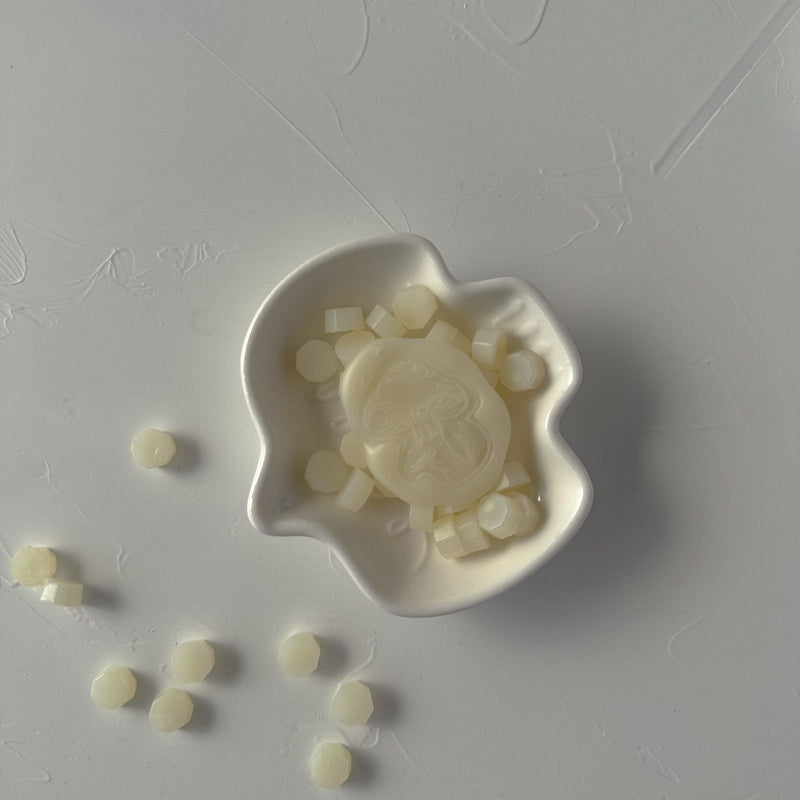 Frosted Ivory Wax Beads shown with a star-design seal mold on a grey surface, soft shimmering detail