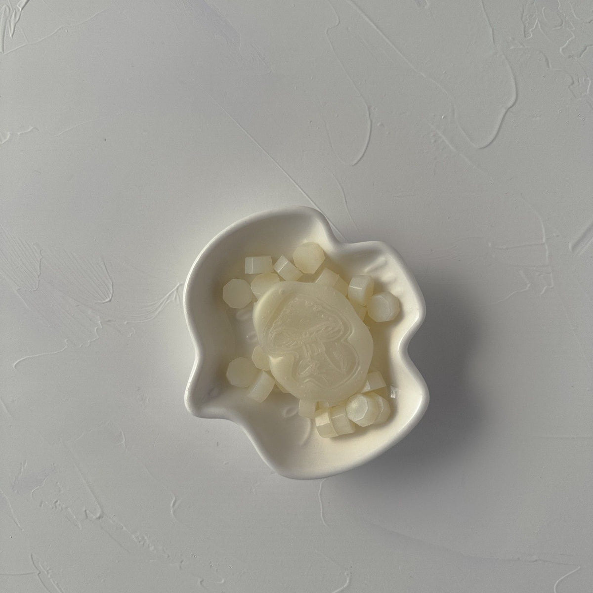 Stamped Frosted Ivory wax seal with a face motif on a white mold, close-up view on a grey surface