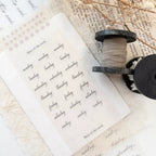Sheet of paper with handwritten days of the week on a textured surface with a spool of thread.