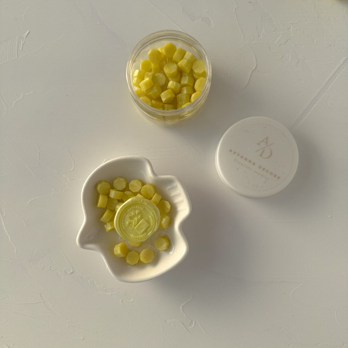 Golden Apple Wax Beads in a jar and white dish showing their golden-yellow glow on a grey background