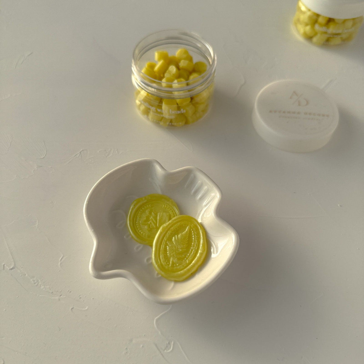 Golden-yellow Golden Apple sealing wax beads filling a jar and small white dish, top view on light grey