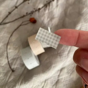 Hand holding a small white box sealed with a Grey Plaid Label Sticker Tape label on beige