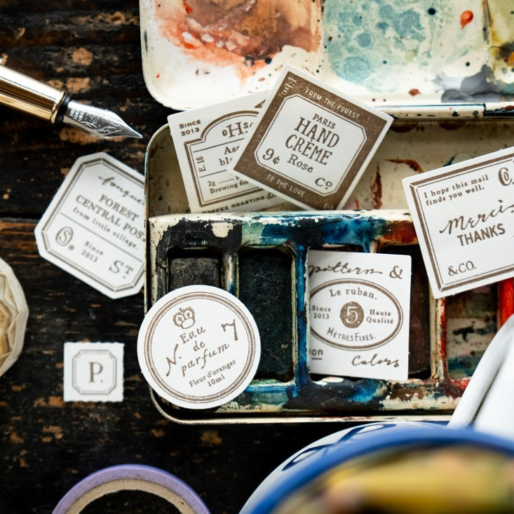 Art supplies including ink bottles, a paint palette, and stationery items on a dark surface.