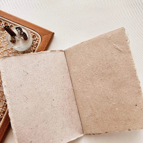 Two textured beige Handmade Paper A6 Notebook pages with a woven mat in the background