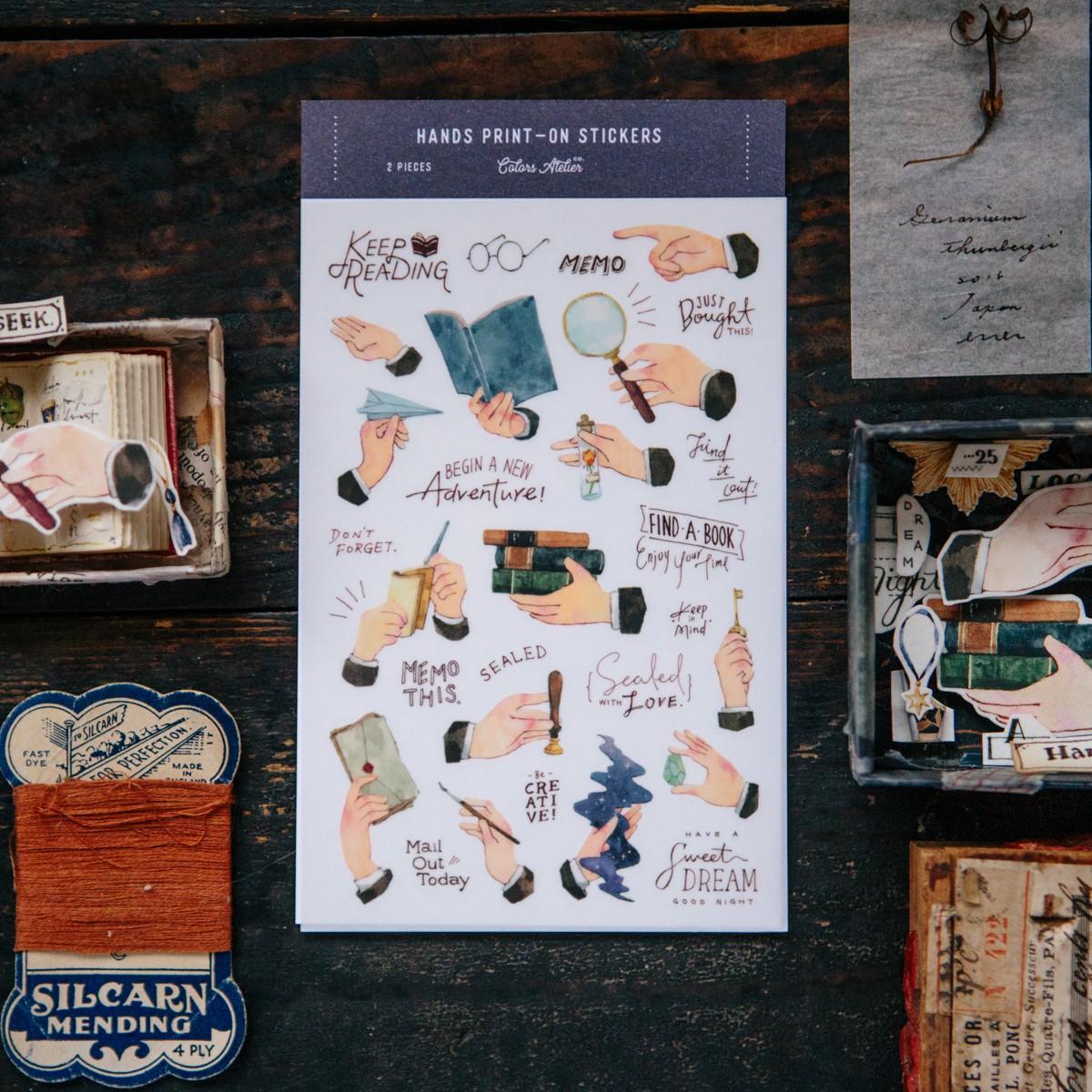 Sheet of decorative stickers with various hand illustrations on a dark wooden surface.