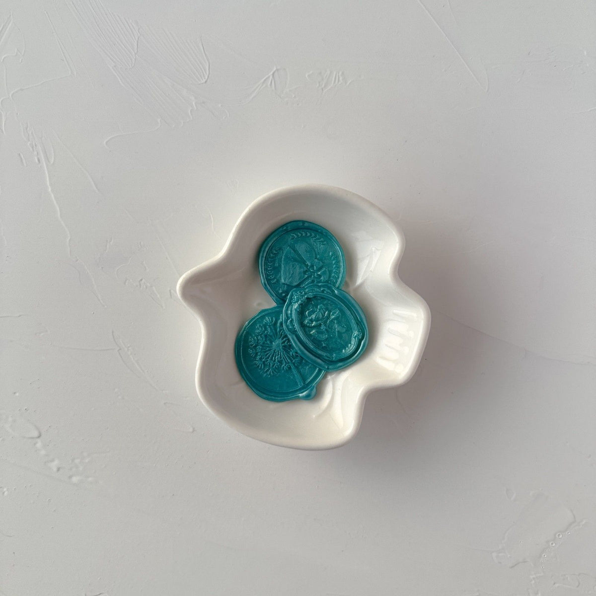 Three melted Hawaiian Blue wax seal discs displayed in a small white dish on a light grey background