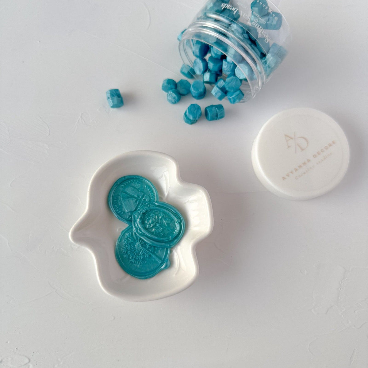 Hawaiian Blue sealing wax beads in a white dish with the full jar behind on a light grey surface
