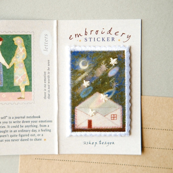 An embroidered sticker card featuring a small stitched house with stars and a moon on the front, labeled 'embroidery STICKER' and signed 'shop teddy'.