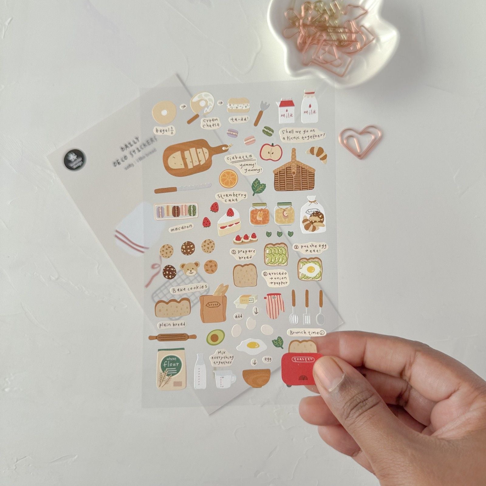 Sheet of decorative stickers with food-themed designs held by a hand on a light background.