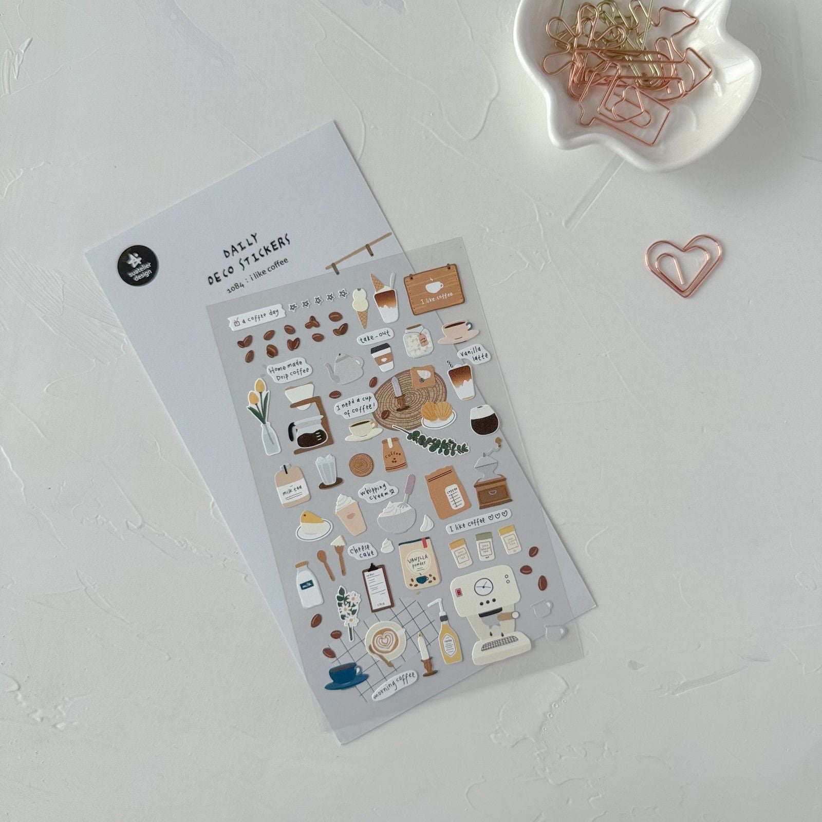 Sticker sheet with coffee-themed designs on a white surface with paper clips.