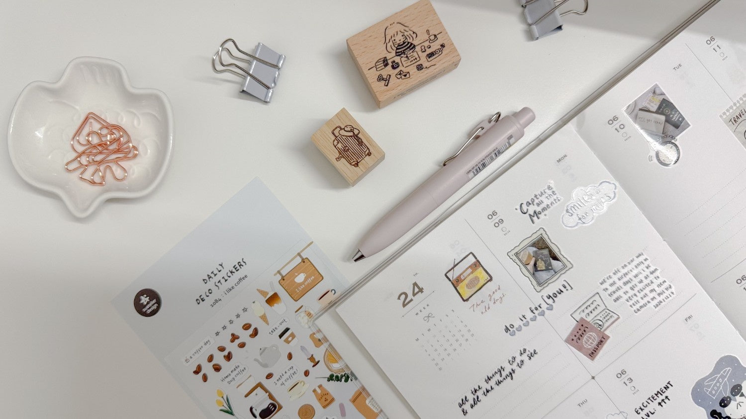Stationery items including a pen, rubber stamps, and paper clips on a desk with a planner open to a page.
