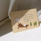 Greeting card with a sunbed, umbrella, and trees illustration on a beige background