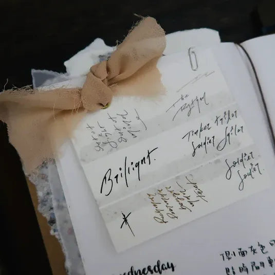 Open book with handwritten notes styled with Addict Washi Tape and a ribbon on a dark backdrop