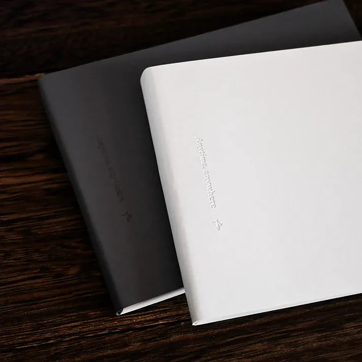 Anytime Anywhere Journal by Jr. Journal in white and dark grey PU leather covers, shown side by side on a wooden desk