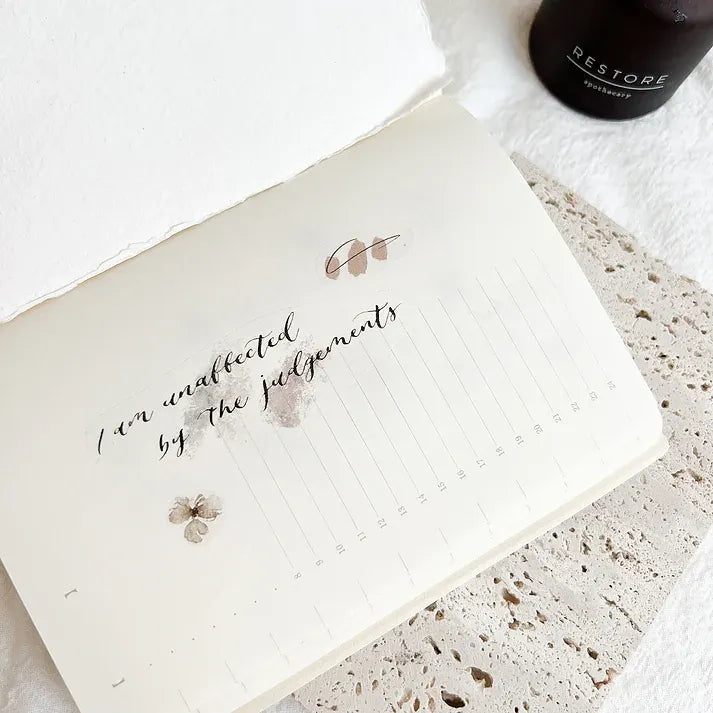 Notebook with handwritten text on a textured surface with a bottle labeled 'RESTORE' in the background.