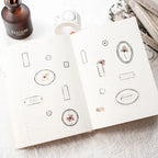 Design sketches of bottle shapes on a white surface with a bottle and books in the background.