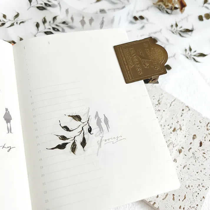 Leaves PET Tape leaf motif on white paper styled with a brown book and textured paper sheets