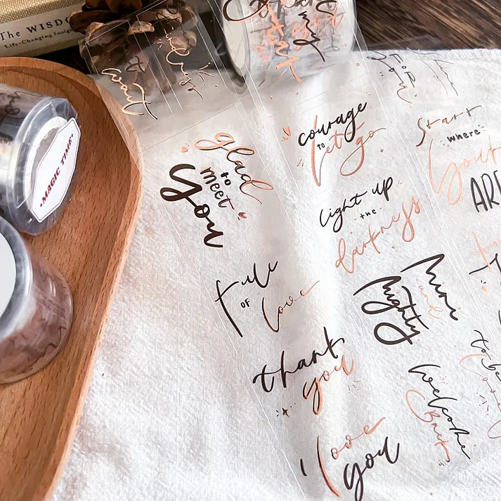 Handwritten-style Magic Time Rose Gold PET Tape quotes applied to white paper on a wooden desk