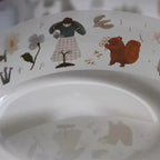 Children's plate with illustrations of a person, a squirrel, and flowers on a white background.