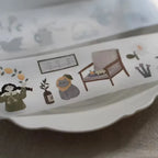 Decorative border with illustrations of a girl, cat, chair, and plants on a white surface.