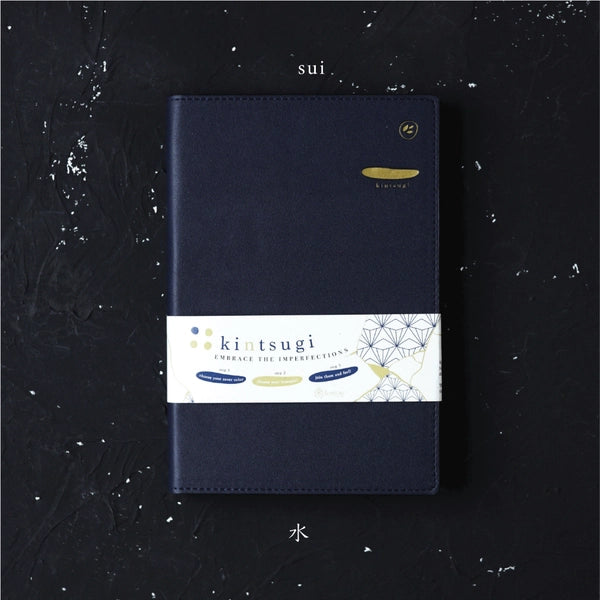 Navy blue notebook with a white label featuring 'kintsugi' on a dark textured background