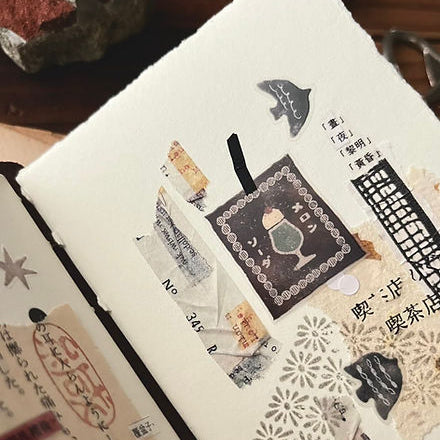 Notebook decorated with Kissaten Cafe Matte PET Tape stickers styled on a warm wooden surface