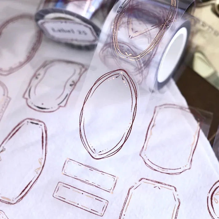 Sheet of gem-shaped Label 25 Rose Gold PET Tape labels with the tape roll visible in the background