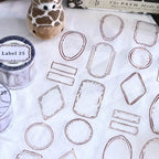 Clear adhesive labels with geometric shapes on a white surface, with a giraffe toy and book in the background.
