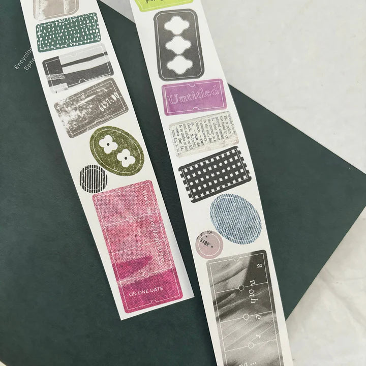 Two strips of Label Paper Label Sticker Tape precut label designs laid on a dark surface