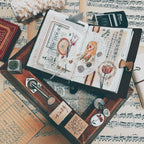 Open book with artistic illustrations on a surface with music sheets and decorative items.