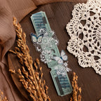 Decorative watch with butterfly design on a wooden surface with lace and dried plants.