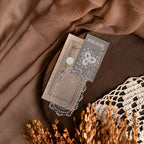 Decorative card with lace design on a wooden surface with fabric and dried flowers.