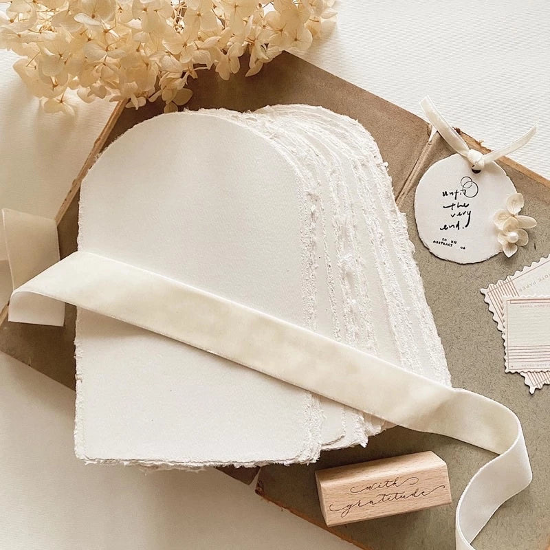 White lace fabric with a ribbon on a textured surface with flowers and cards.