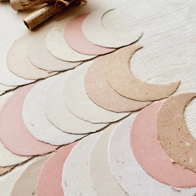Set of crescent moon-shaped paper cutouts in various colors on a light wooden surface.