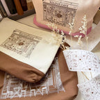 Textile items with 'Kolour Cafe' design on a surface with dried plants.
