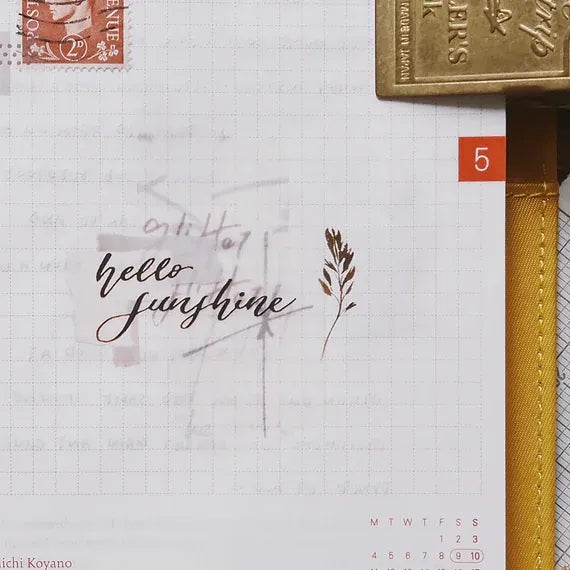 Notebook page with a hello sunshine Latte PET Tape phrase, a stamp and gold pen styled on top