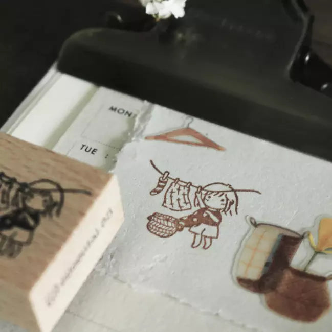 Mini Girls Laundry stamp beside a small illustrated notebook on a dark styled surface
