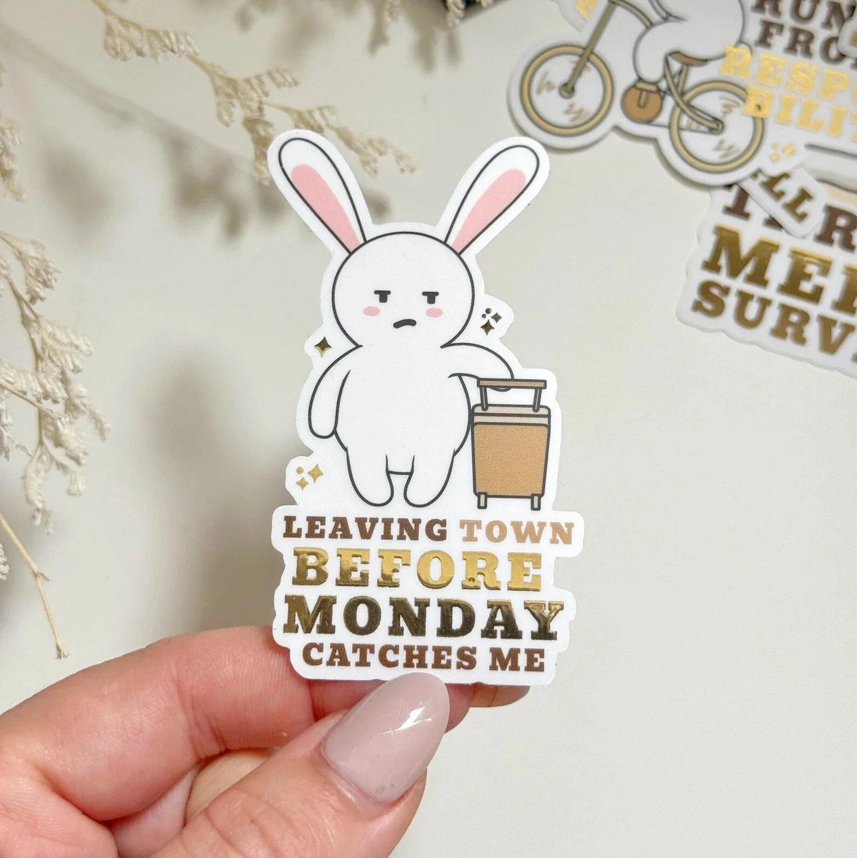 Sticker with a cartoon rabbit holding a suitcase and text 'Leaving town before Monday catches me' held by a hand.