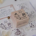 Wooden stamp with cartoon design on a surface with stamped images and stationery items.