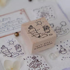 Wooden stamp with cartoon design on a surface with stamped images and stationery items.