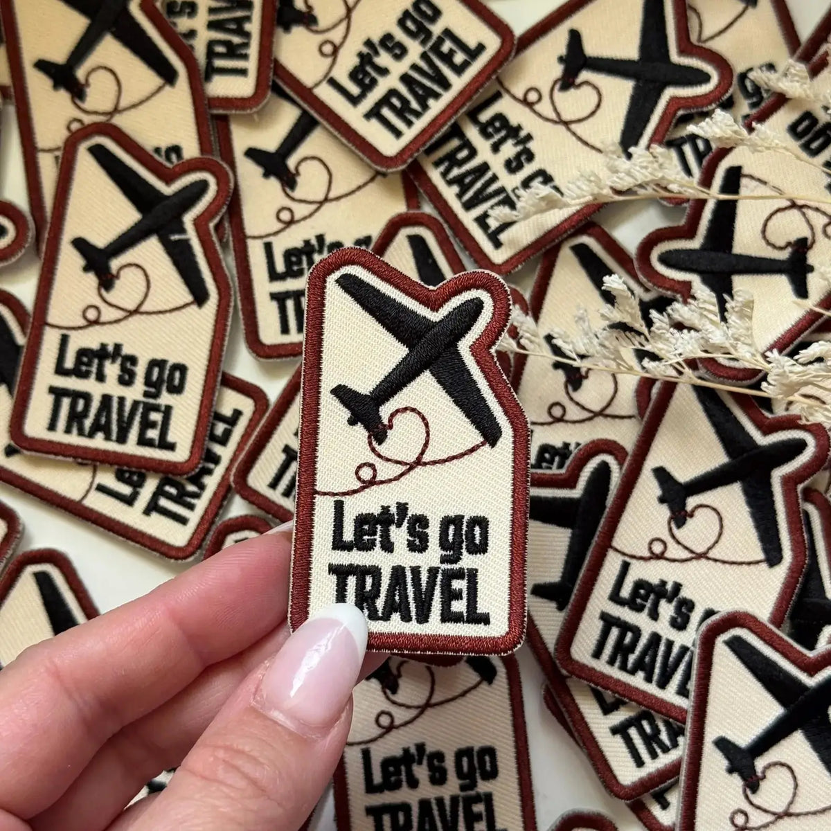 Hand holding Let's Go Travel Embroidered Patches with airplane icons, more patches around