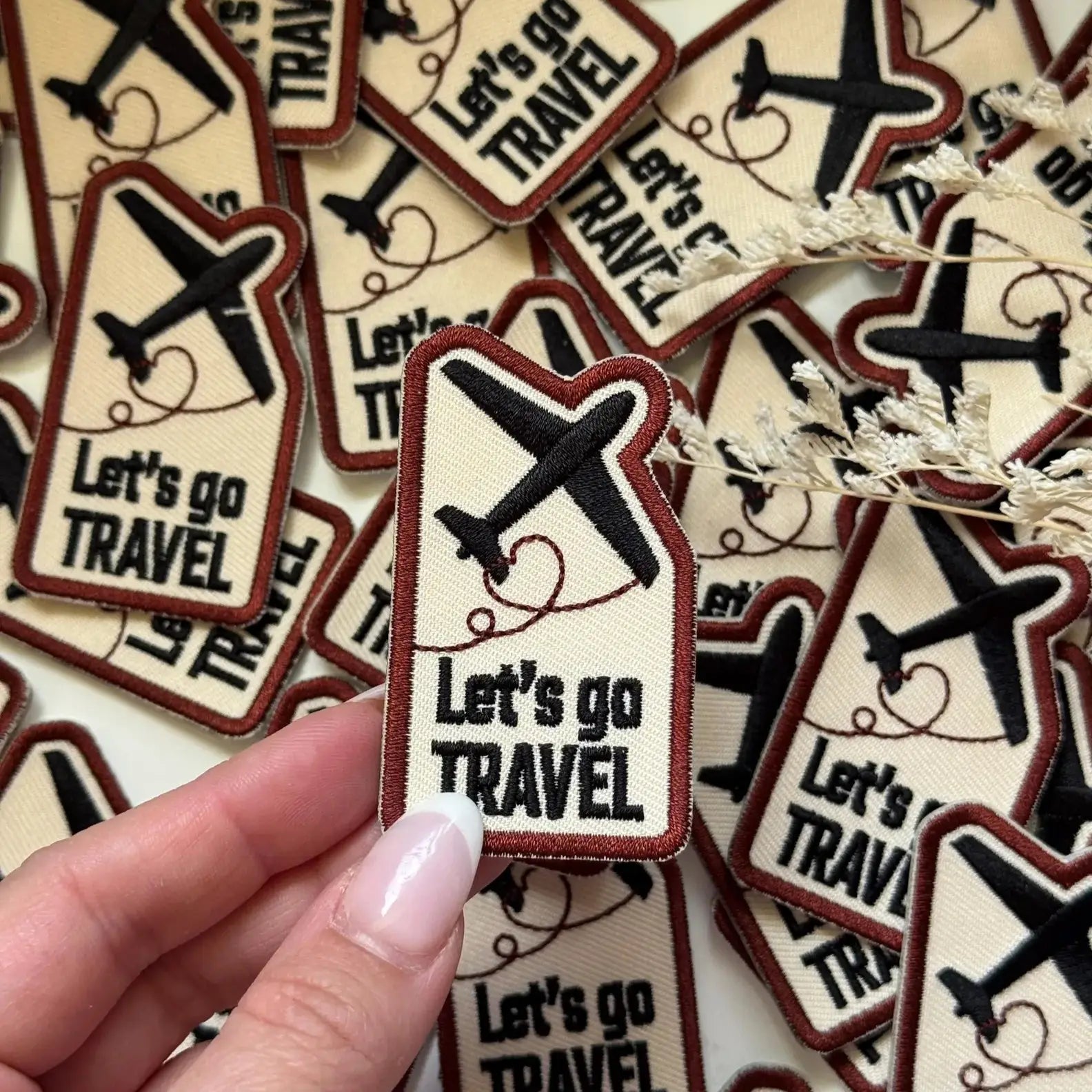 Collection of 'Let's go TRAVEL' patches with airplane icons, held by a hand.
