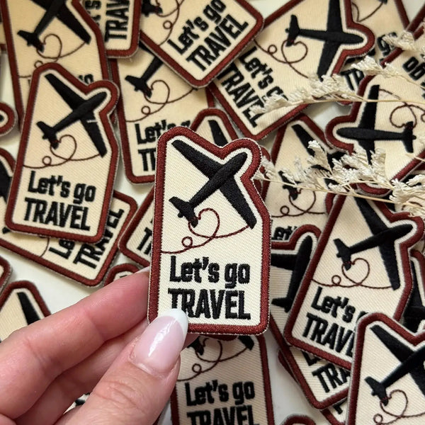 Hand holding Let's Go Travel Embroidered Patches with airplane icons, more patches around